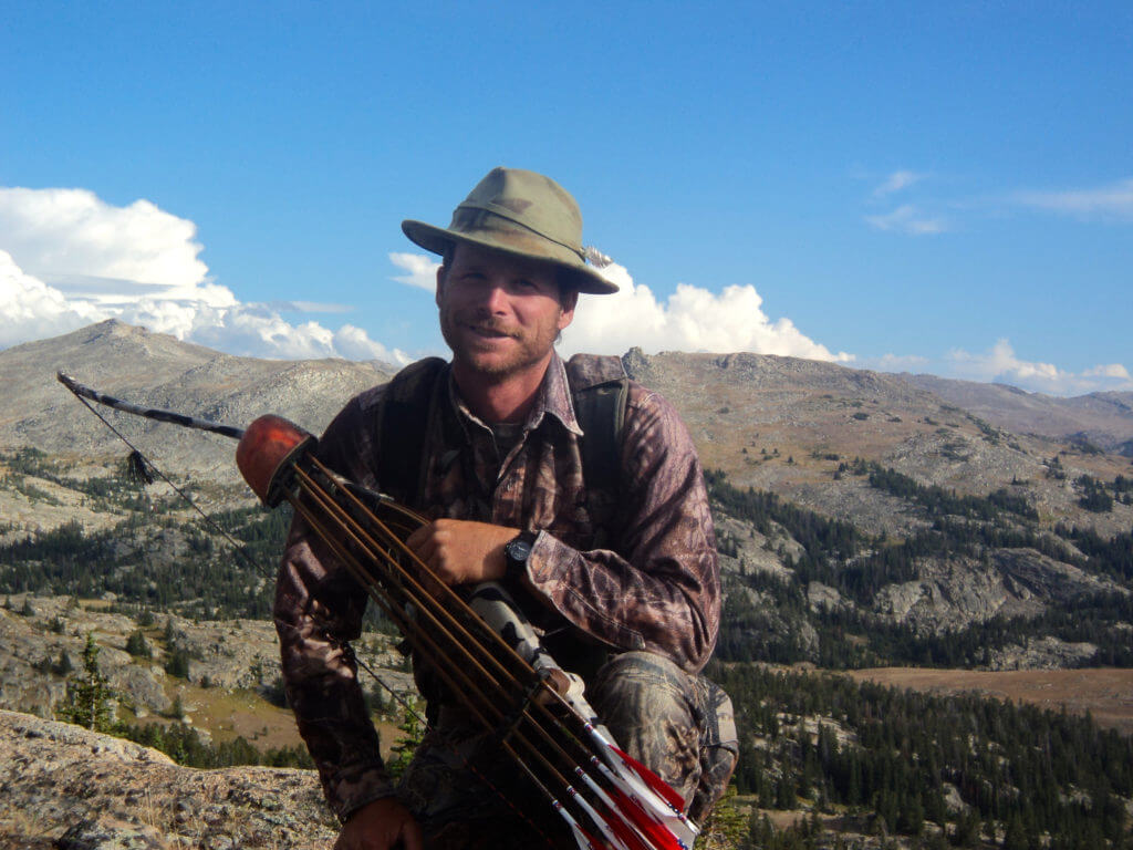 Hunter with bow and quiver posing in front of mountain range