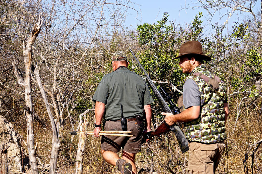 Hunters trekking through thick vegetation looking for buffalo